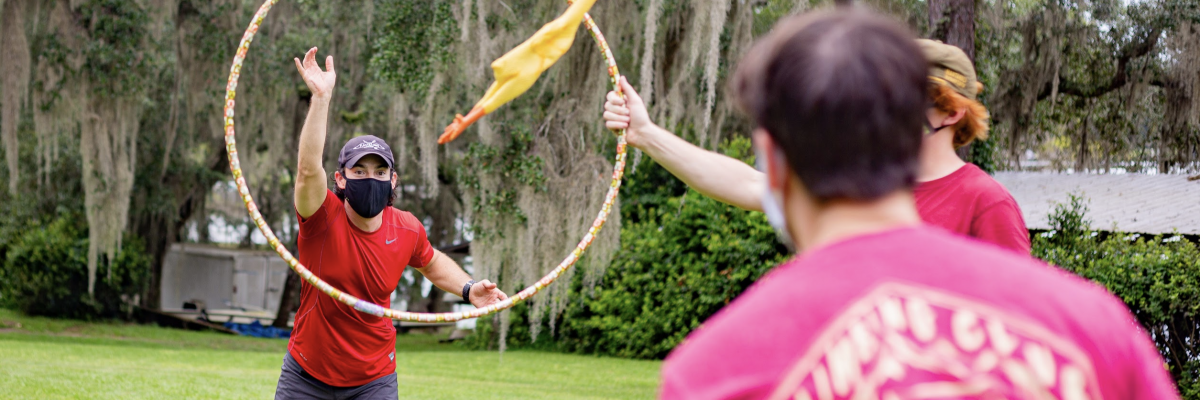 Masked participate throws a rubber chicken through a hula hoop.