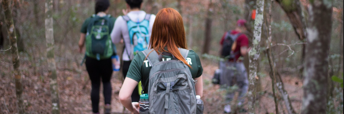 A red haired women wearing a backpack walks down a wooded trail