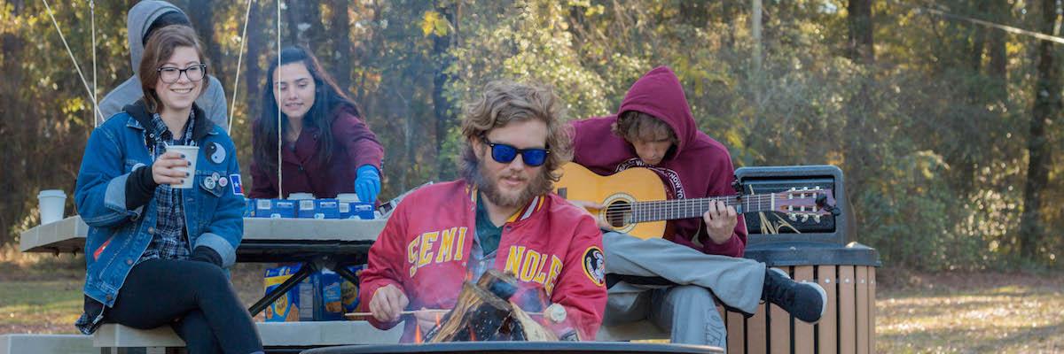 Students sitting on a picnic table roast marshmallow and sip hot chocolate