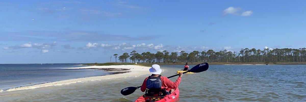 Student in red kayak paddling in shallow water