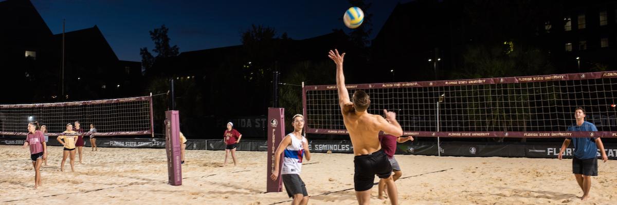 Male students playing sand volleyball at night
