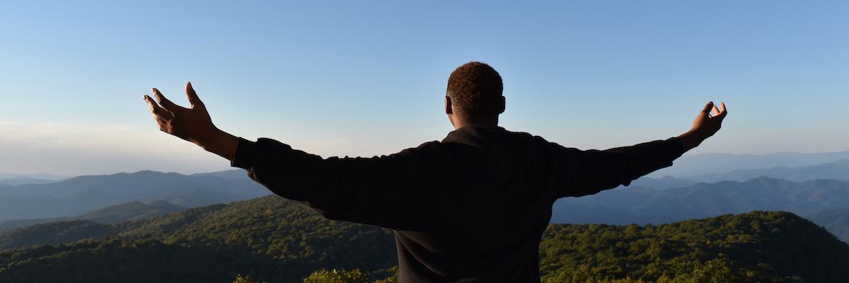 male student looking out over the mountains with his arms out