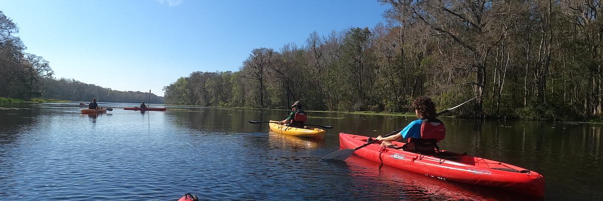 students in kayaks paddling down a river
