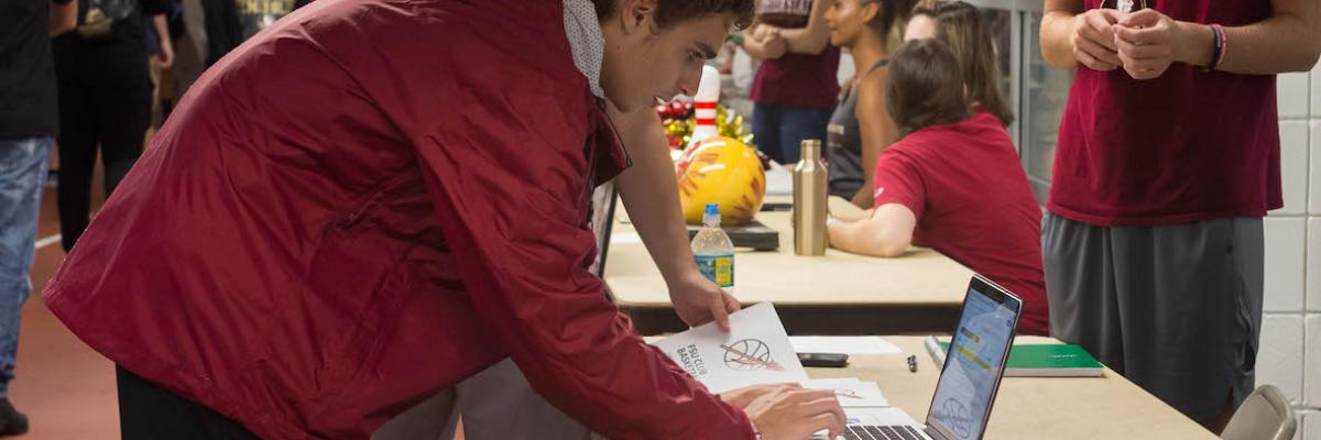 male student leaning down towards laptop to type