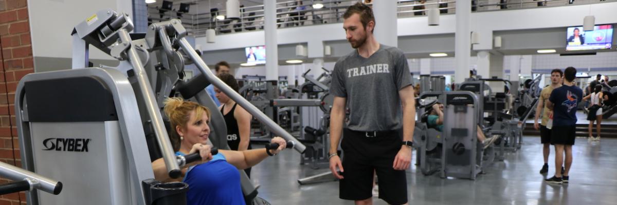 Male trainer coaching female client on chest press machine in the gym