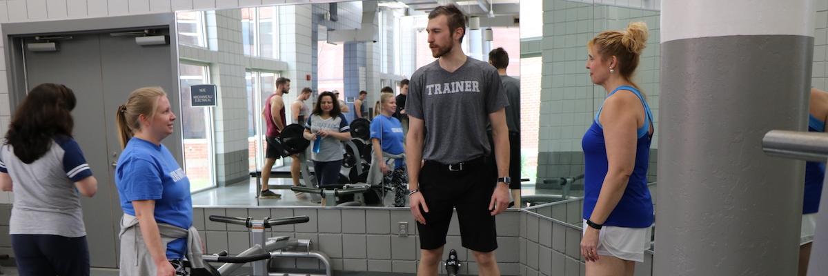 Male trainer coaching two female clients in weight room