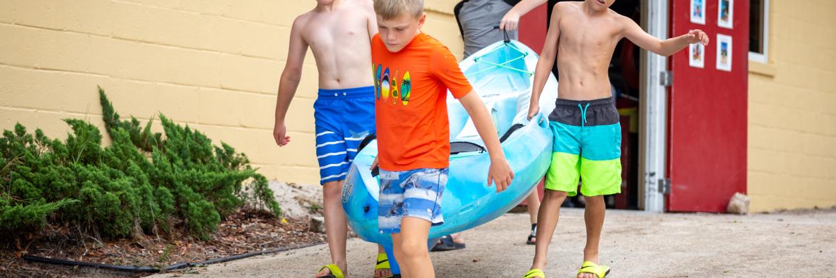 campers carrying a kayak to the water at Camp Flastacowo