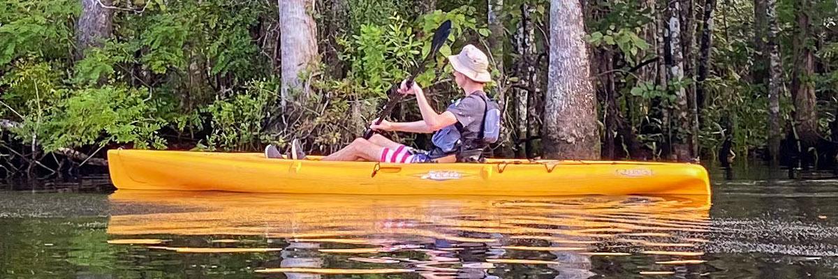 An outdoor pursuits participant kayaks down Wacissa River in an orange kayak