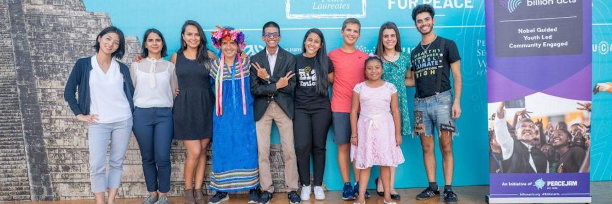 A group of students, winners of the Billion Acts of Peace Hero Award, stand in a row on stage.