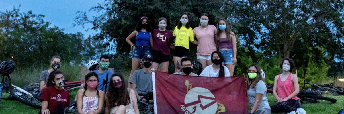 Students grouped on the grass, wearing masks, and holding an Outodor P