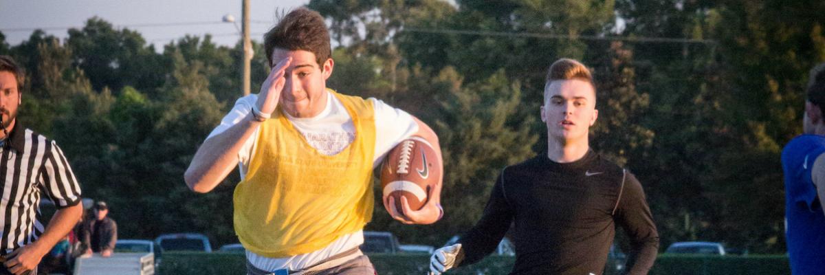 A flag football player in a yellow jersey runs with a football