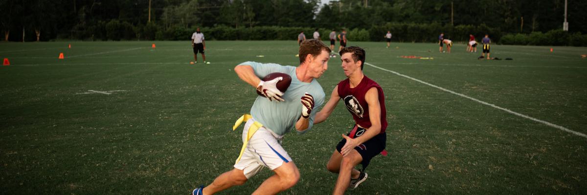 A flag football player holding a football is running past another player
