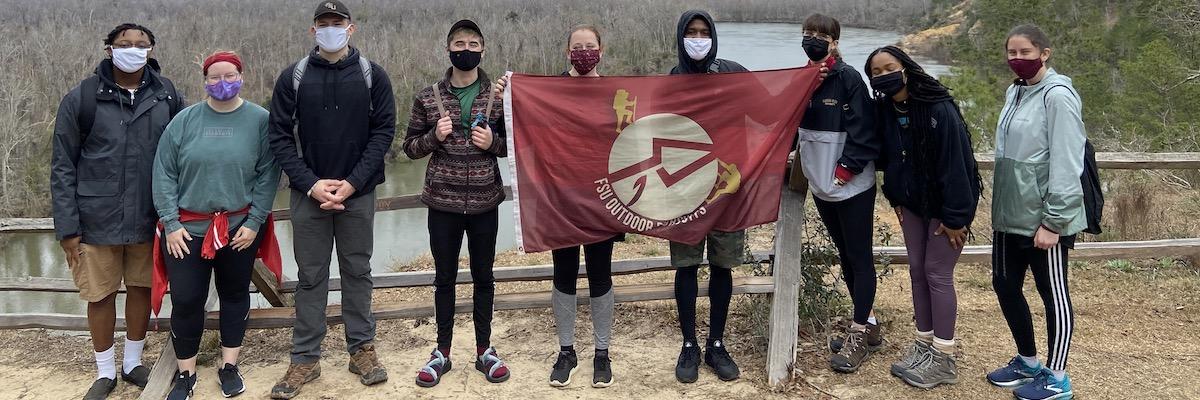 A group of FSU students stand in front of a scenic vista, holding the Outdoor Pursuits flag