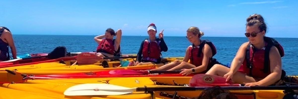 Four students in kayaks rest near each other in a bay