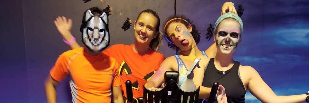 Spin Instructors dressed in Halloween costumes pose behind a spin bike