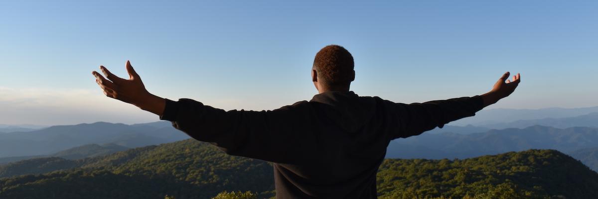 Male student overlooking mountain with his arms out