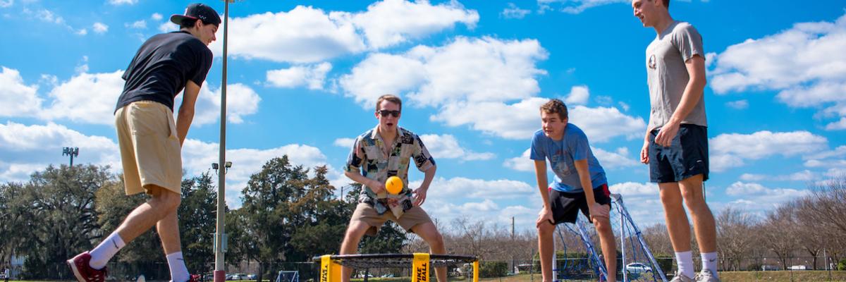 Four male students playing spike ball game outside