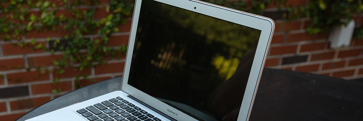 MacBook laptop open on black table outdoors with brick wall and ivy in background