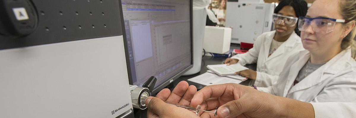 Image of chemistry students wearing lab coats and working in lab on new computer and technical equipment