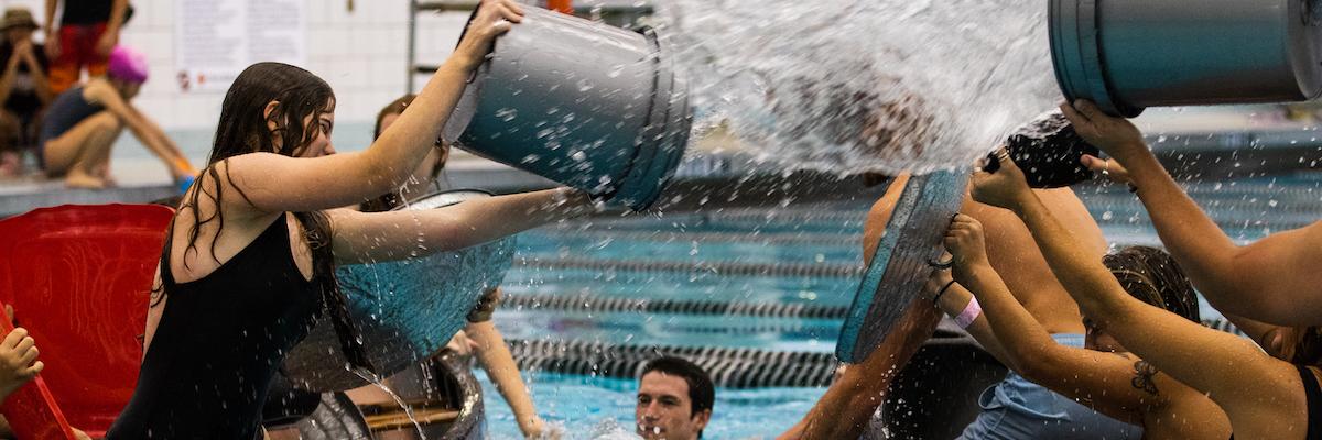 students in canoes in the Leach pool, using trash cans to dump water on each other