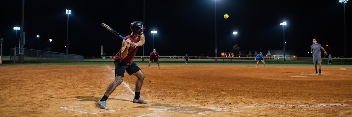 student on softball field, swinging the bat at the ball coming towards him