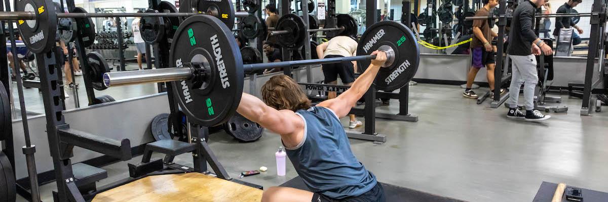 Male student performing an olympic lift, squatting and holding a barbell above his head