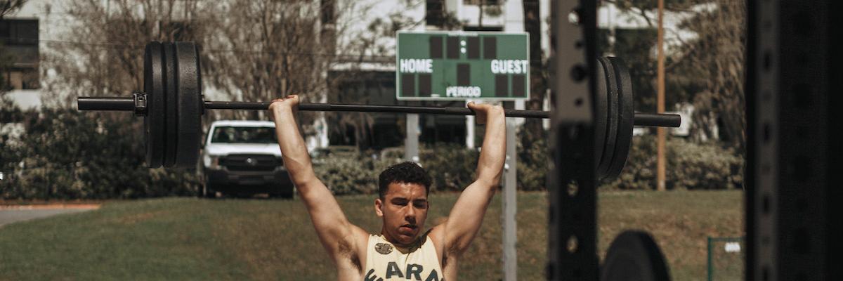 Male student lifting a barbell with weights above his head