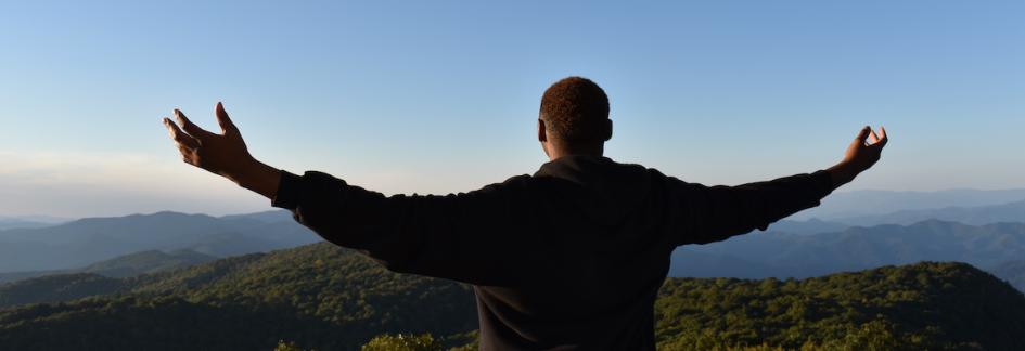 male student looking out over the mountains with his arms out